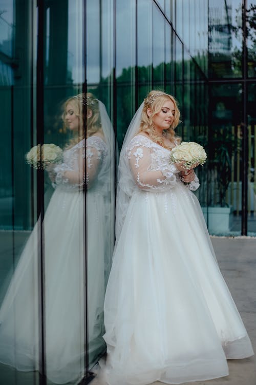 Bride Holding Bouquet of Flowers near Glass Wall