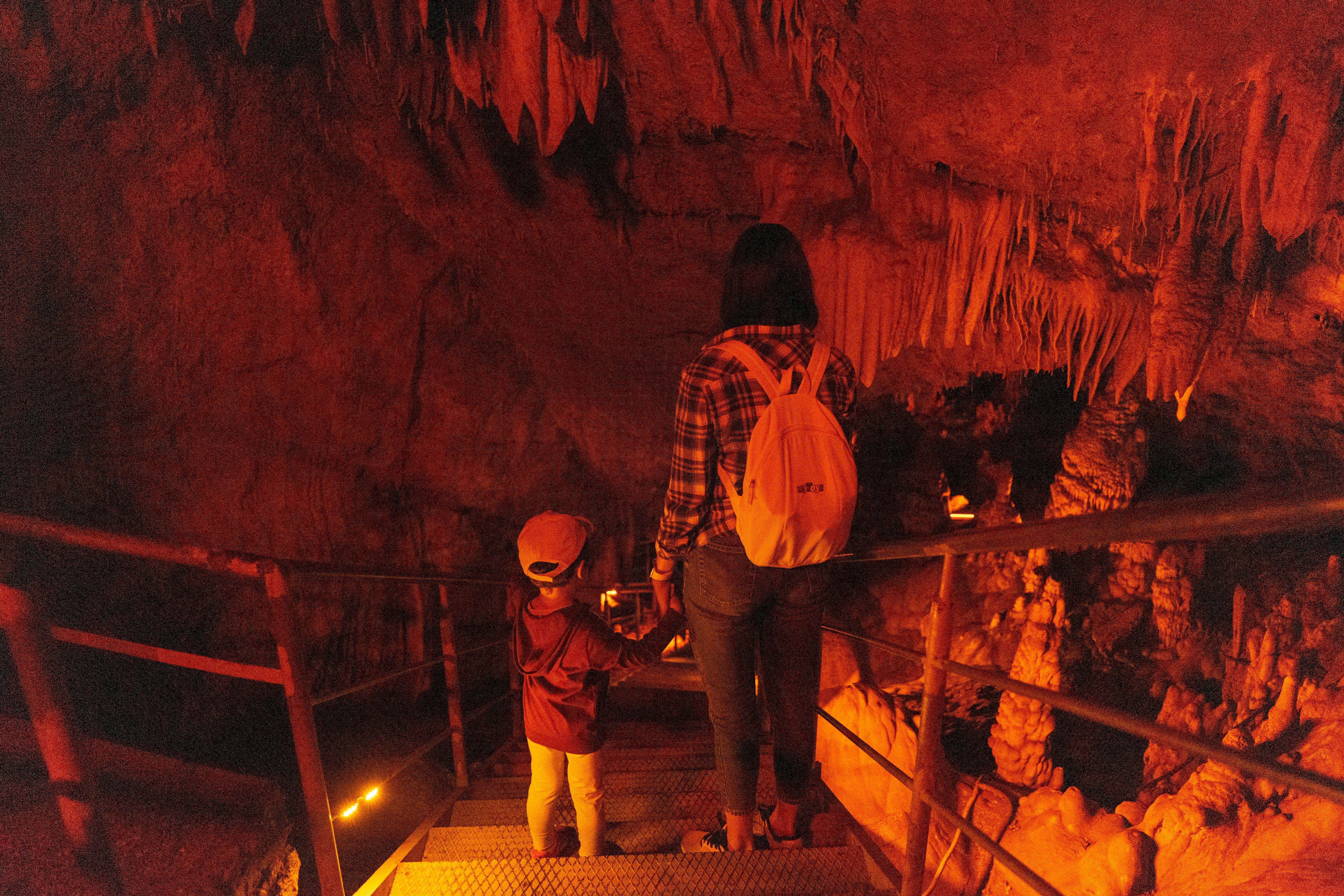 A mother and child descending stairs in a dimly lit cave, surrounded by stalactites.