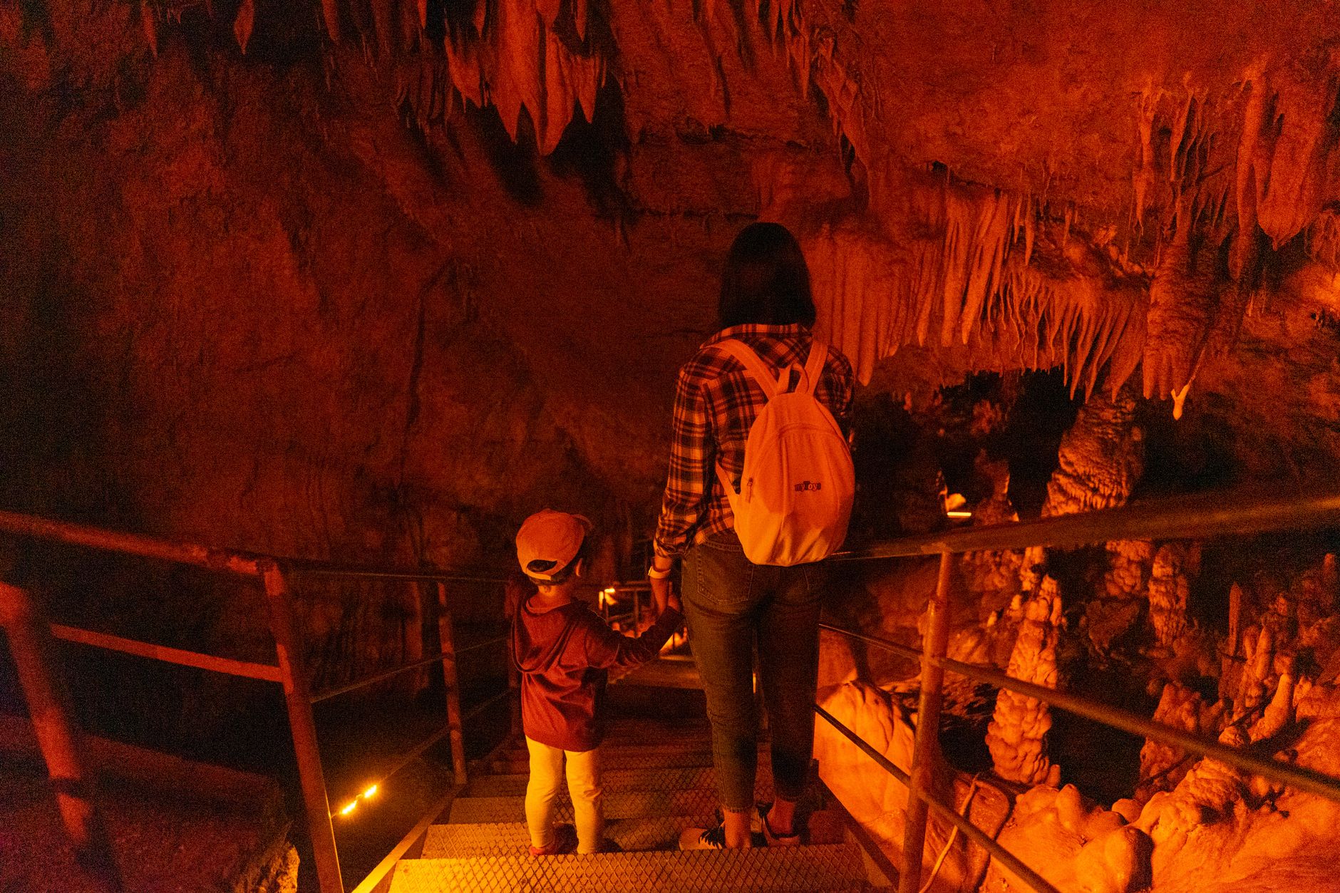 A mother and child descending stairs in a dimly lit cave, surrounded by stalactites.