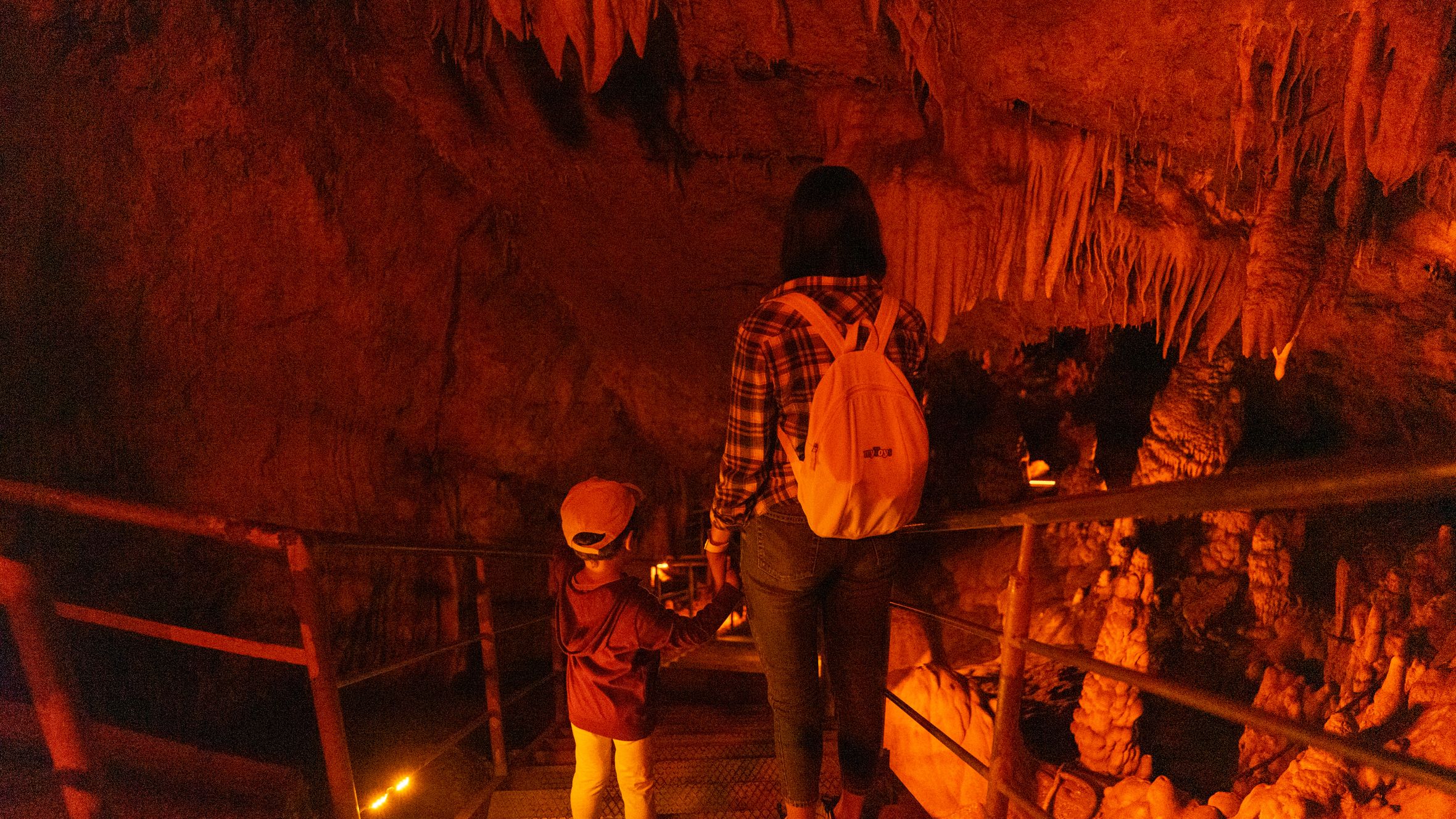 A mother and child descending stairs in a dimly lit cave, surrounded by stalactites.