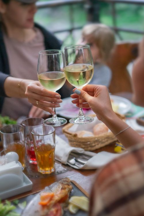 Free A lively outdoor gathering featuring a toast with white wine glasses over a dining table. Stock Photo
