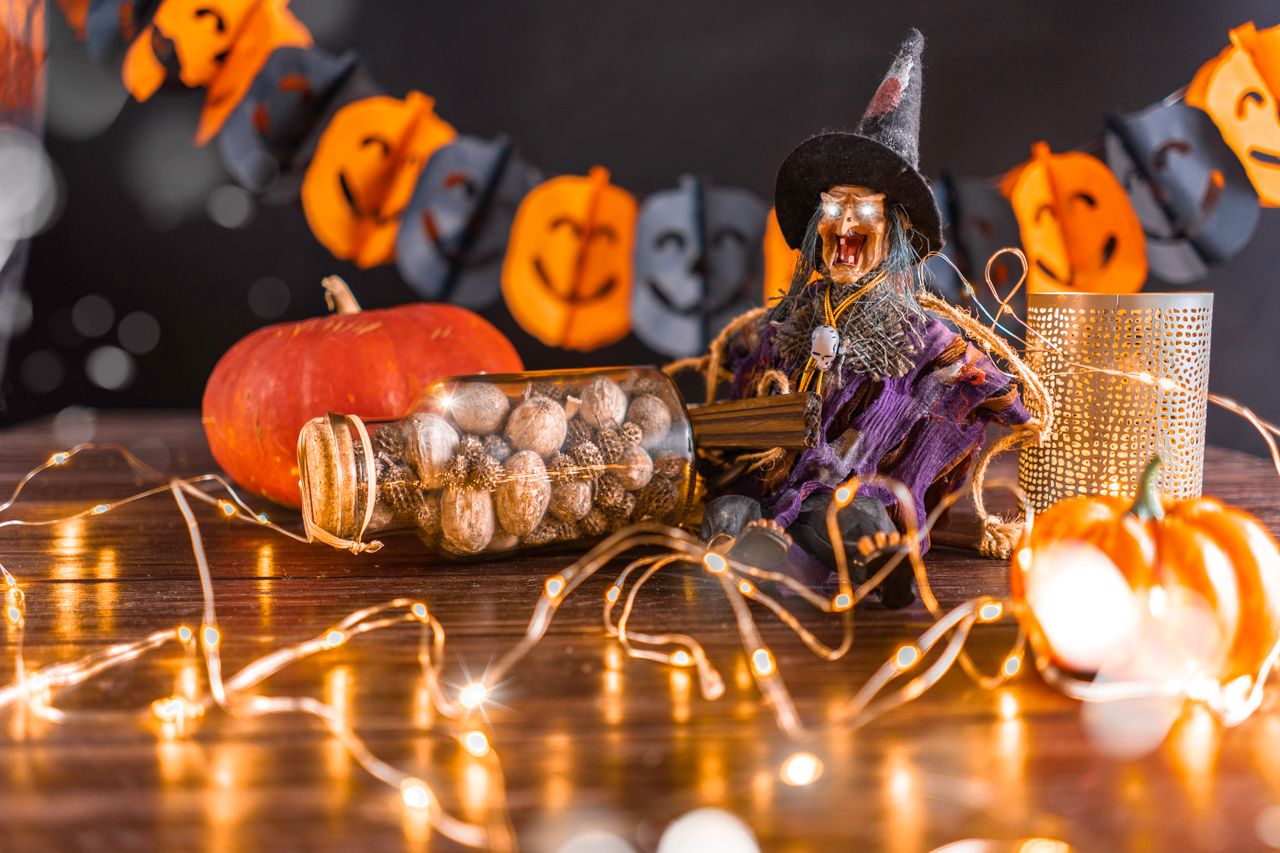 Witch figurine on a table with a jar of nuts, pumpkins, fairy lights, and a pumpkin garland behind