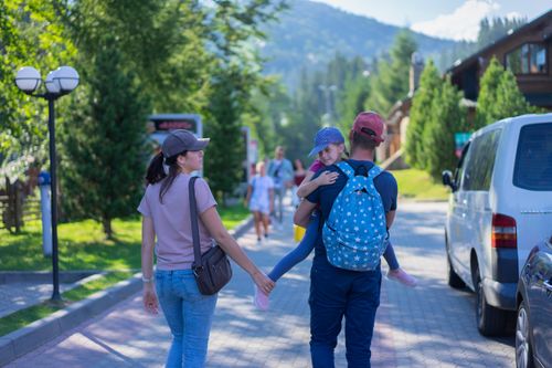 Free Parents walking with their daughter in a picturesque mountain village, enjoying a sunny day outdoors. Stock Photo