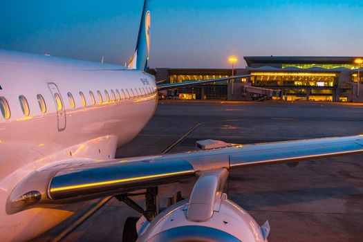 A commercial airplane parked at an illuminated airport terminal during dusk, showcasing modern aviation travel.