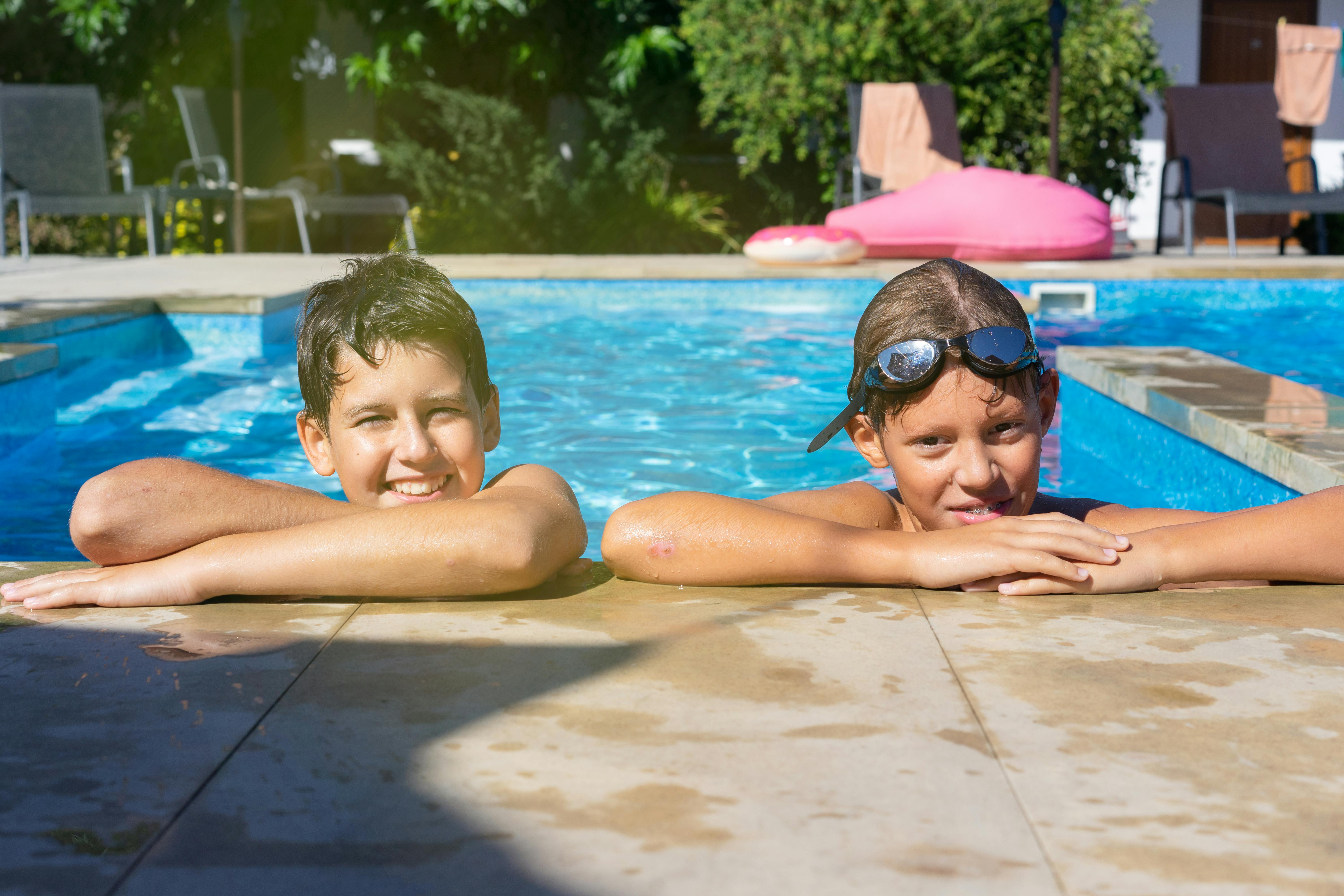 Two kids smiling and relaxing in a swimming pool, enjoying a sunny vacation day.