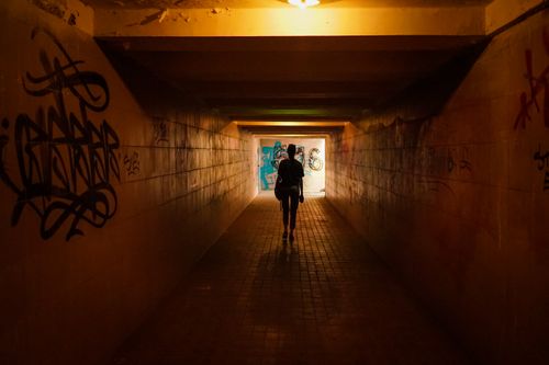 Free A silhouette of a person walking in a dimly lit graffiti-filled urban tunnel. Stock Photo