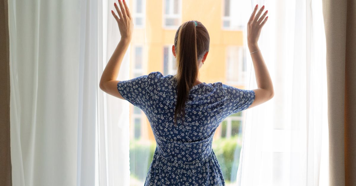 Person standing by a bright window stretching in the morning sunlight