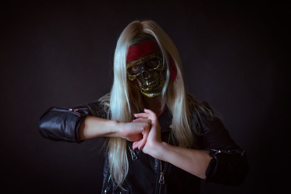 Portrait of a person wearing a skull mask and black leather jacket against a dark background.
