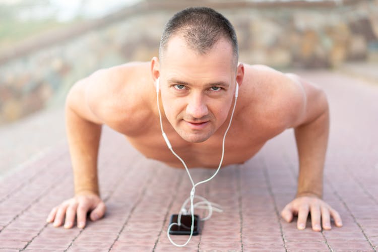 A Shirtless Man Doing Push Ups While Listening To Music