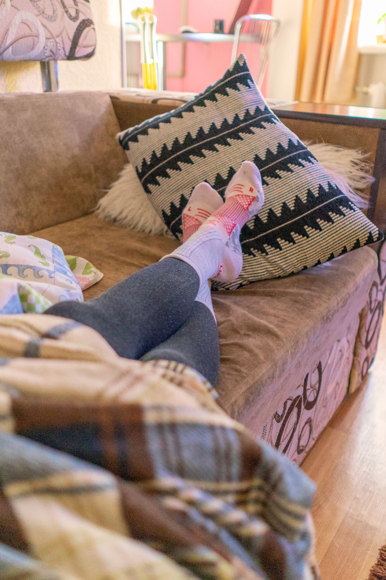 Person relaxing on a sofa with a plaid blanket and a patterned throw pillow