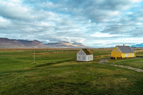 A White and Yellow House on Green Grass Field Near the Mountain Under the Cloudy Sky