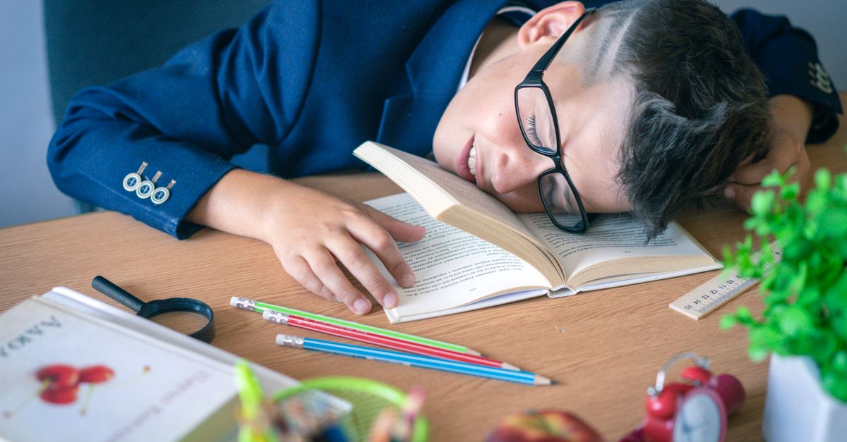 Student studying at a desk with a clock showing 8 PM, looking exhausted with coffee cup nearby
