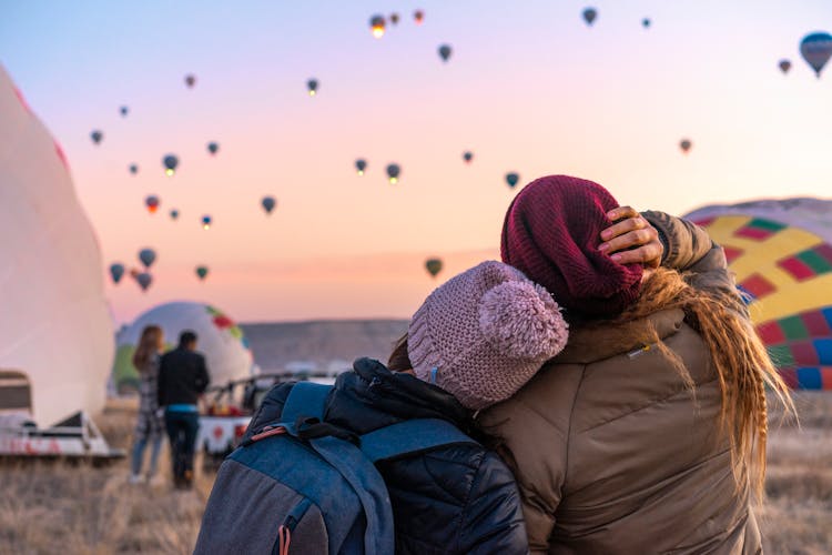 Friends Hugging Looking At Hot Air Balloons Flying In Sky