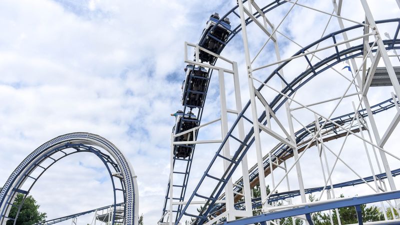 Experience the adrenaline rush of a steel roller coaster under blue skies at an amusement park.