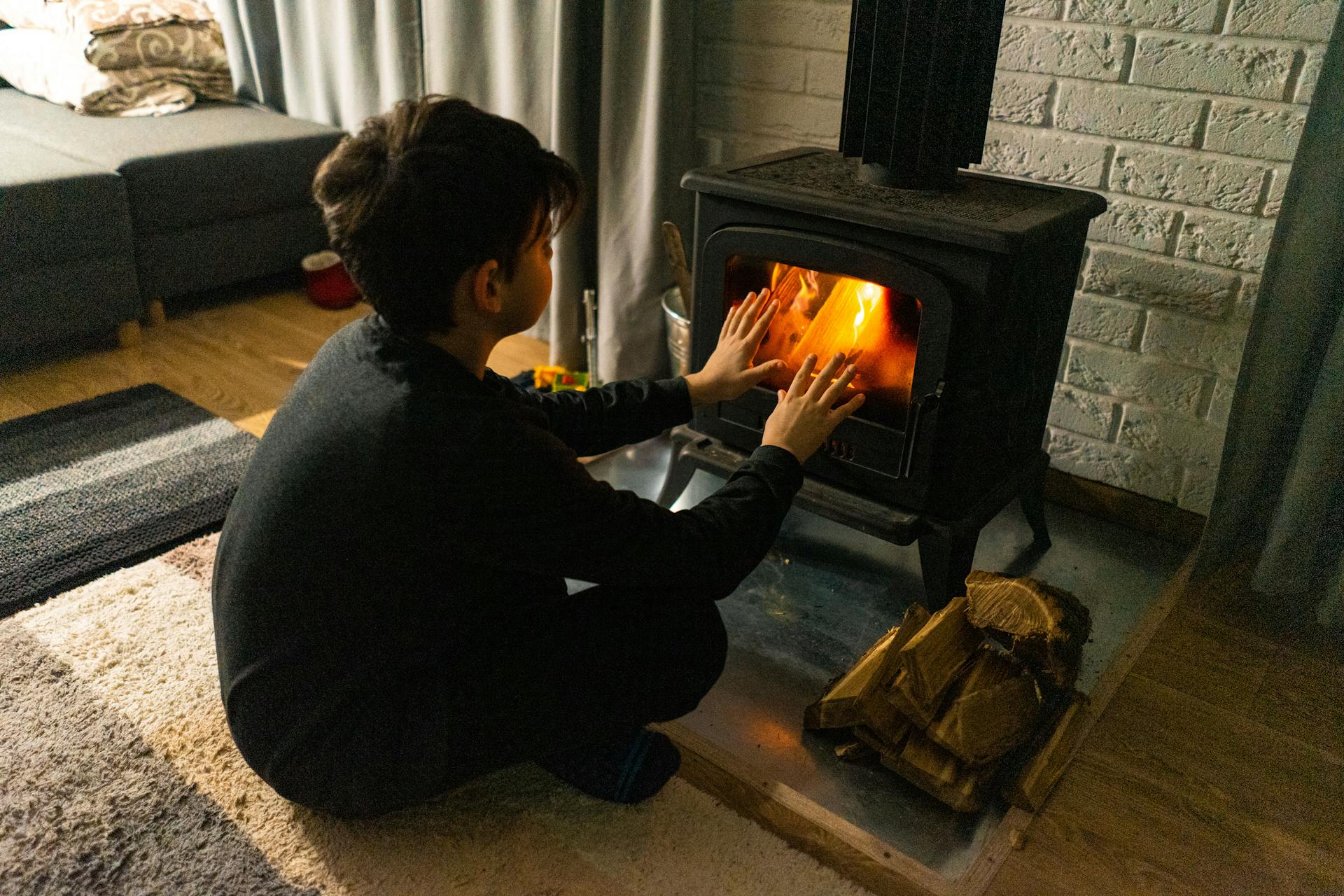 A child warms hands by a wood stove in a cozy living room, creating a warm winter ambiance.