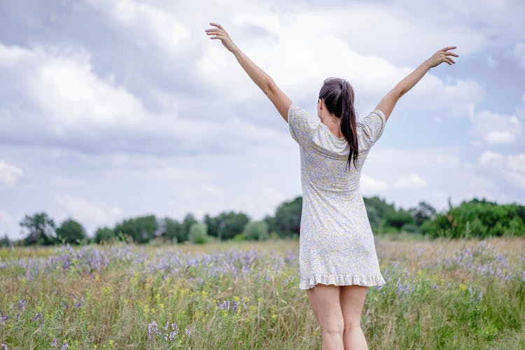 Young Woman With Her Arms Spread On A Field In Summer