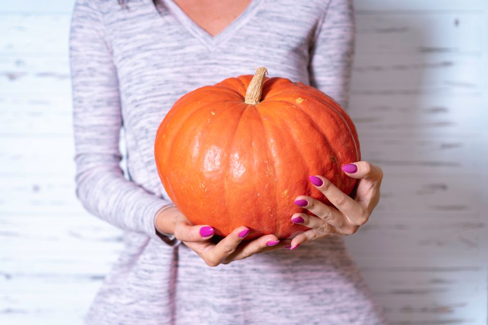 Close-up of woman holding a pumpkin, emphasizing the harvest and autumn season.
