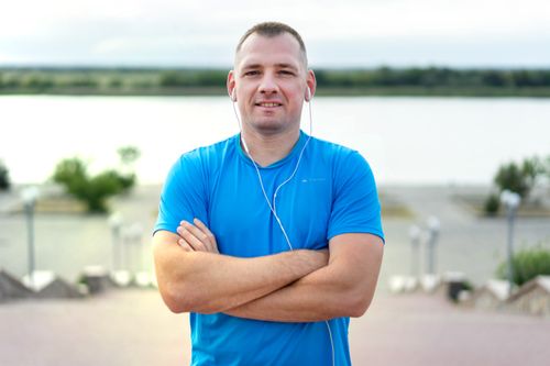 Free Smiling man in blue t-shirt listening to music by the lake. Relaxed and happy mood. Stock Photo