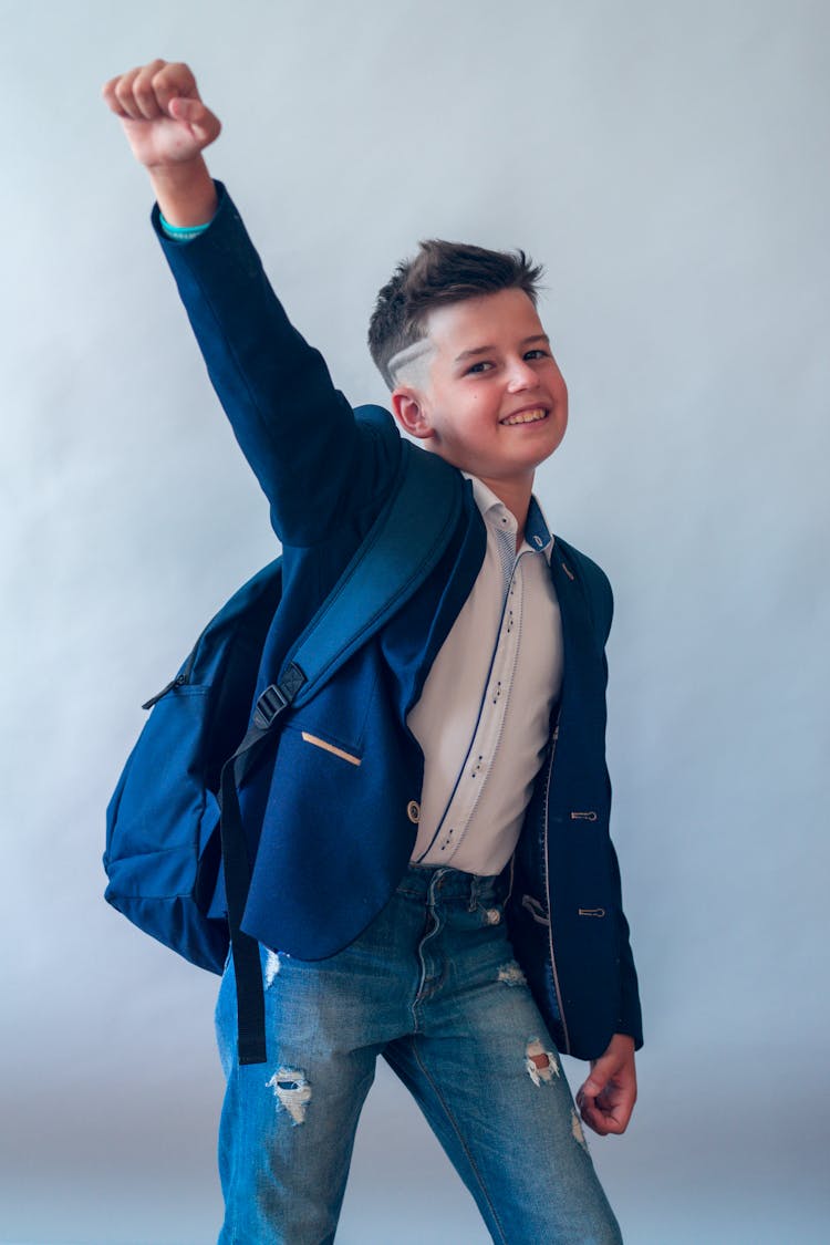 Photograph Of A Kid With A Backpack Raising His Hand