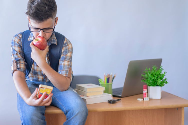 Boy Sitting On Table While Eating An Apple