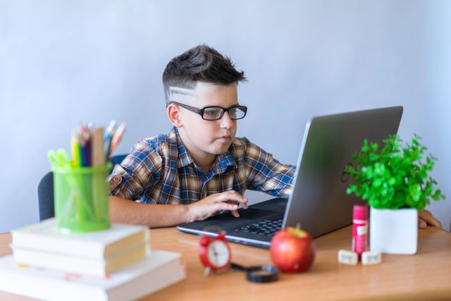 A young student in glasses following an online lesson