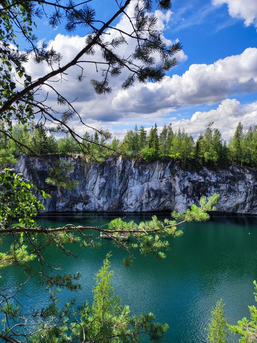 Free A serene lake surrounded by lush greenery and majestic cliffs under a vibrant blue sky. Stock Photo