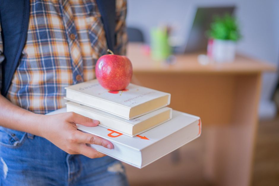 Child holding books with an apple in a classroom, symbolizing education.