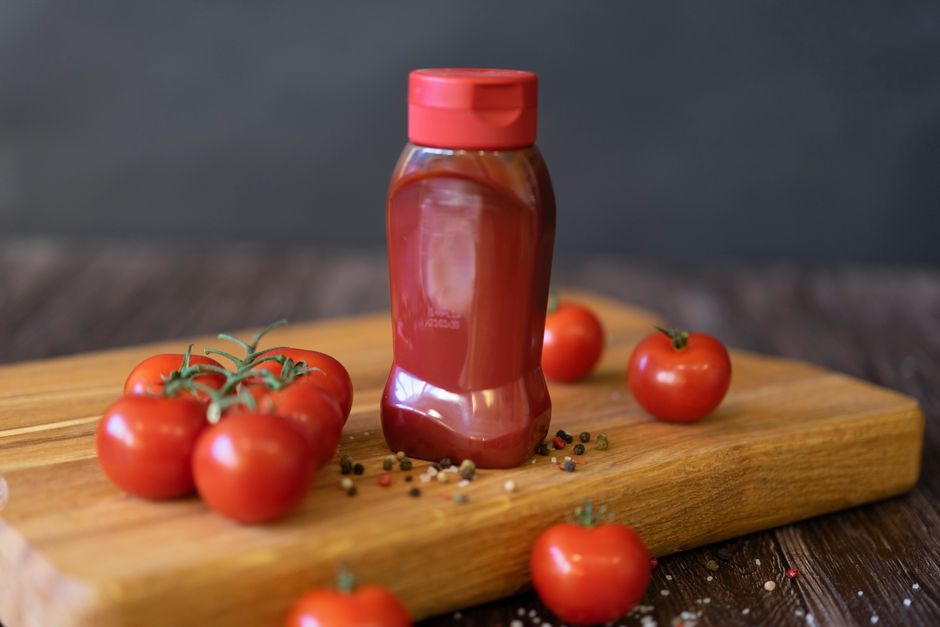 Homemade passata in a glass bottle surrounded by fresh tomatoes