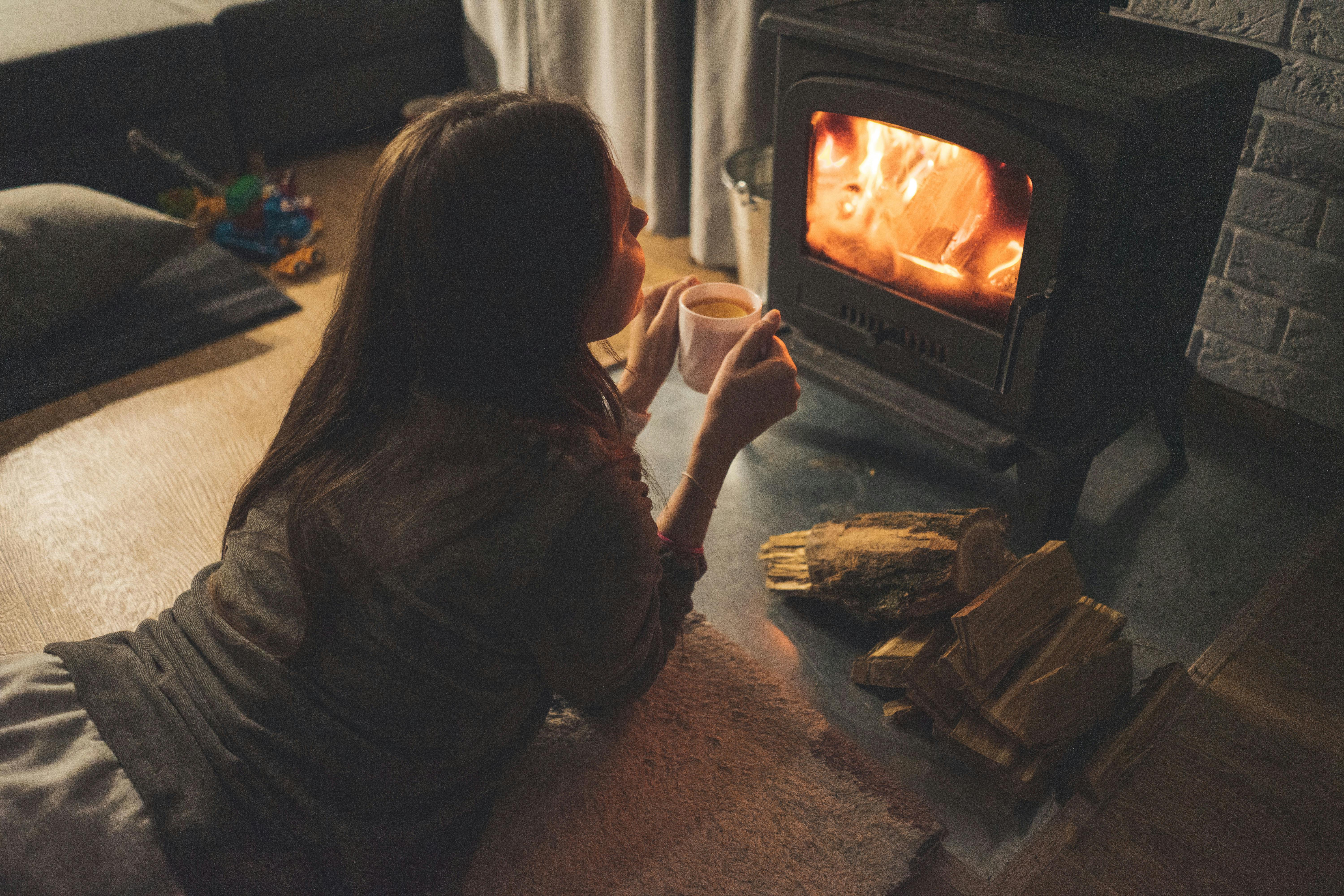 Woman Lying Down on Floor Holding a Cup of Coffee Near Hearth
