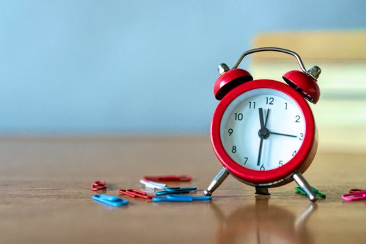 Red alarm clock and colorful paper clips on a wooden desk in a close-up view.