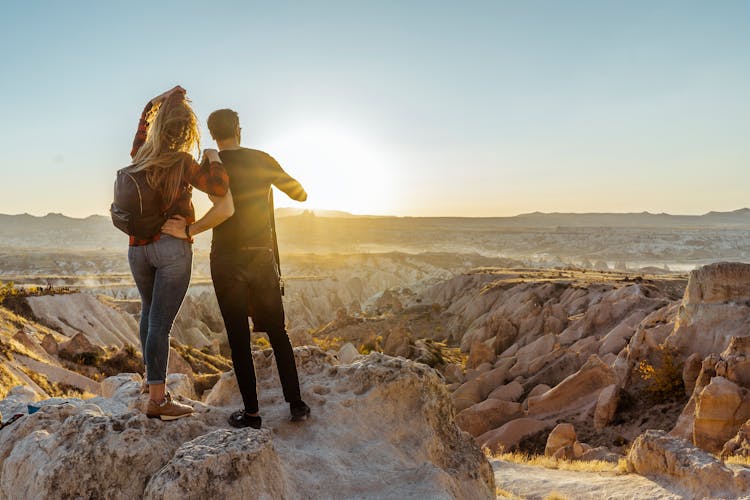 Man And Woman Standing And Looking At The Sunrise In The Mountains