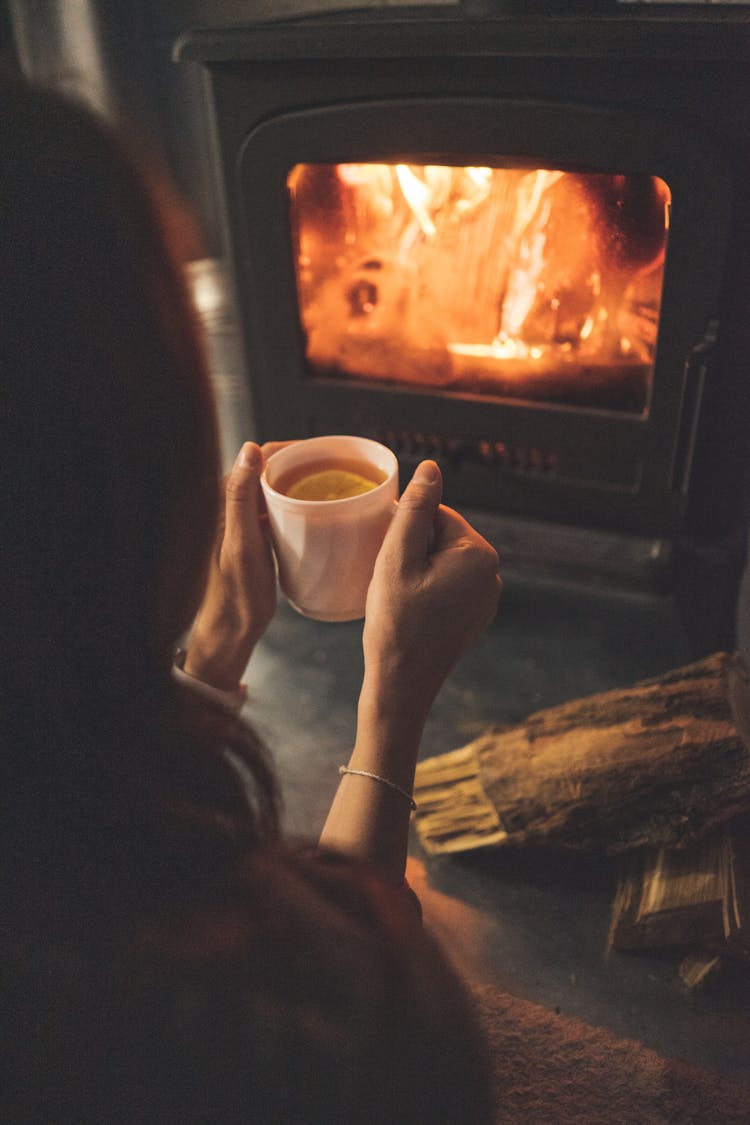 Woman Sitting With Tea Near Fireplace At Home