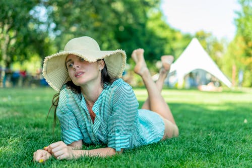 Woman in Green and White Stripe Dress Shirt Wearing Sun Hat Lying Down on Grass