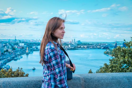 Free Woman in checkered shirt enjoys river view from urban vantage point. Scenic city background. Stock Photo