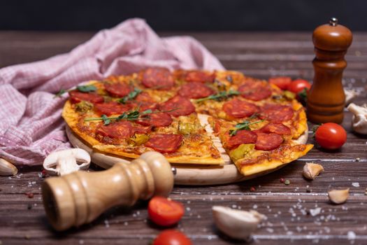 Delicious pepperoni pizza on a wooden board with fresh tomatoes and garlic on a rustic table.