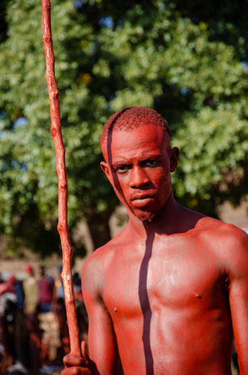 Shirtless Man with Skin Painted Red Holding a Stick During a Ritual