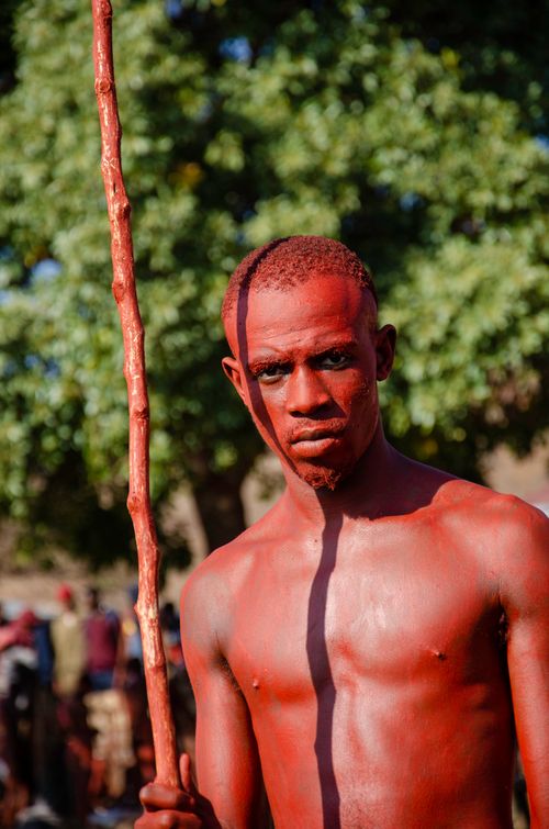 Free Shirtless man covered in red with a stick in traditional celebration outdoors. Stock Photo