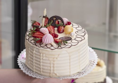 Close-up of a beautifully decorated vanilla cream cake topped with fresh strawberries and elegant chocolate details.