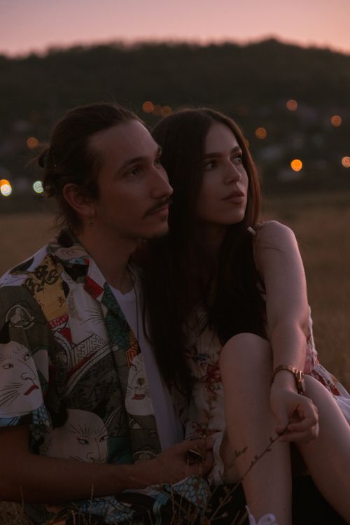 Free A young couple sitting together in a field during sunset, embracing a moment of love and connection. Stock Photo