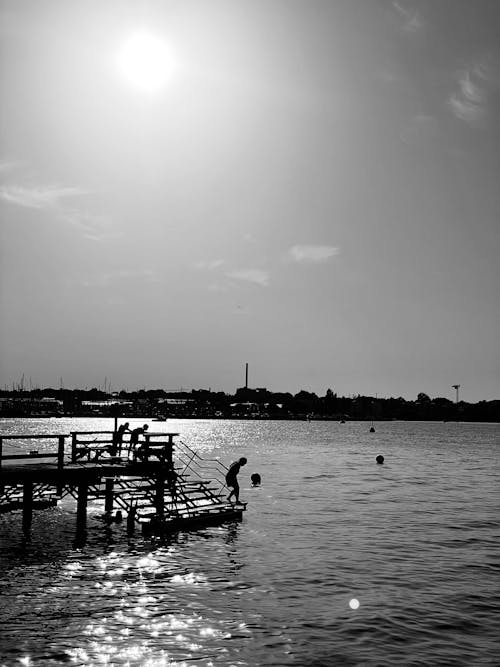 A Grayscale Photo of People on Dock Near Body of Water