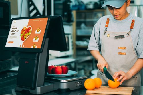 Free A cafe worker slicing oranges at a counter with a digital menu display. Stock Photo