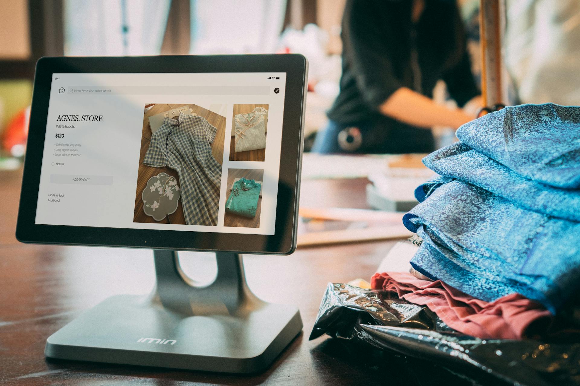 A digital point-of-sale system in a small fashion boutique with clothes displayed on a tablet.