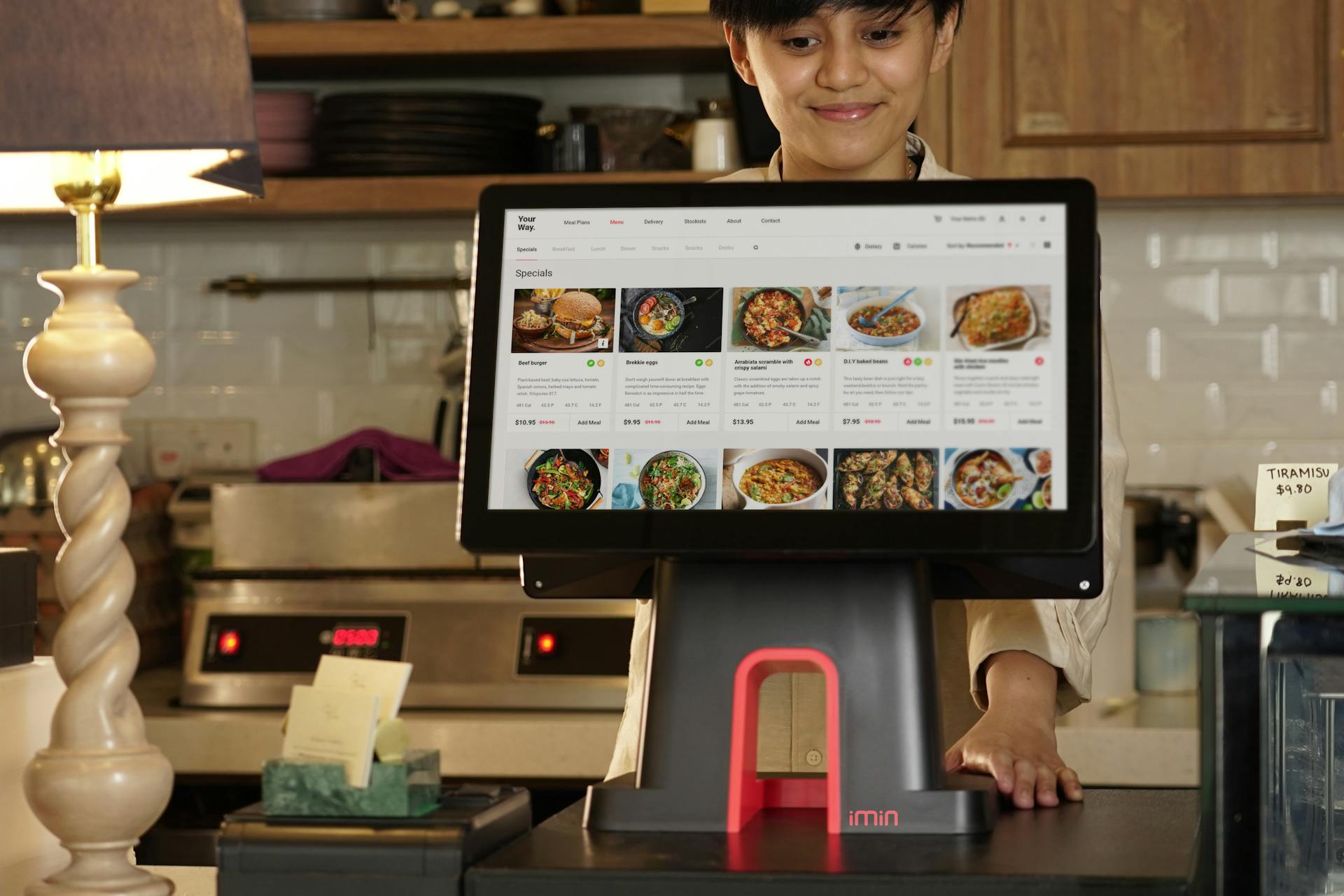 A cashier uses a touchscreen system for taking orders in a restaurant setting.