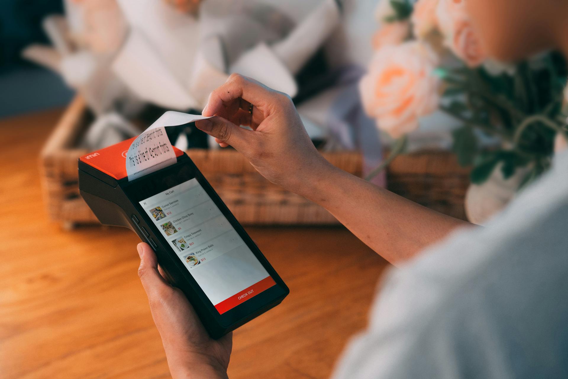 Close-up of a cashless payment transaction using a modern payment terminal indoors with a floral background.