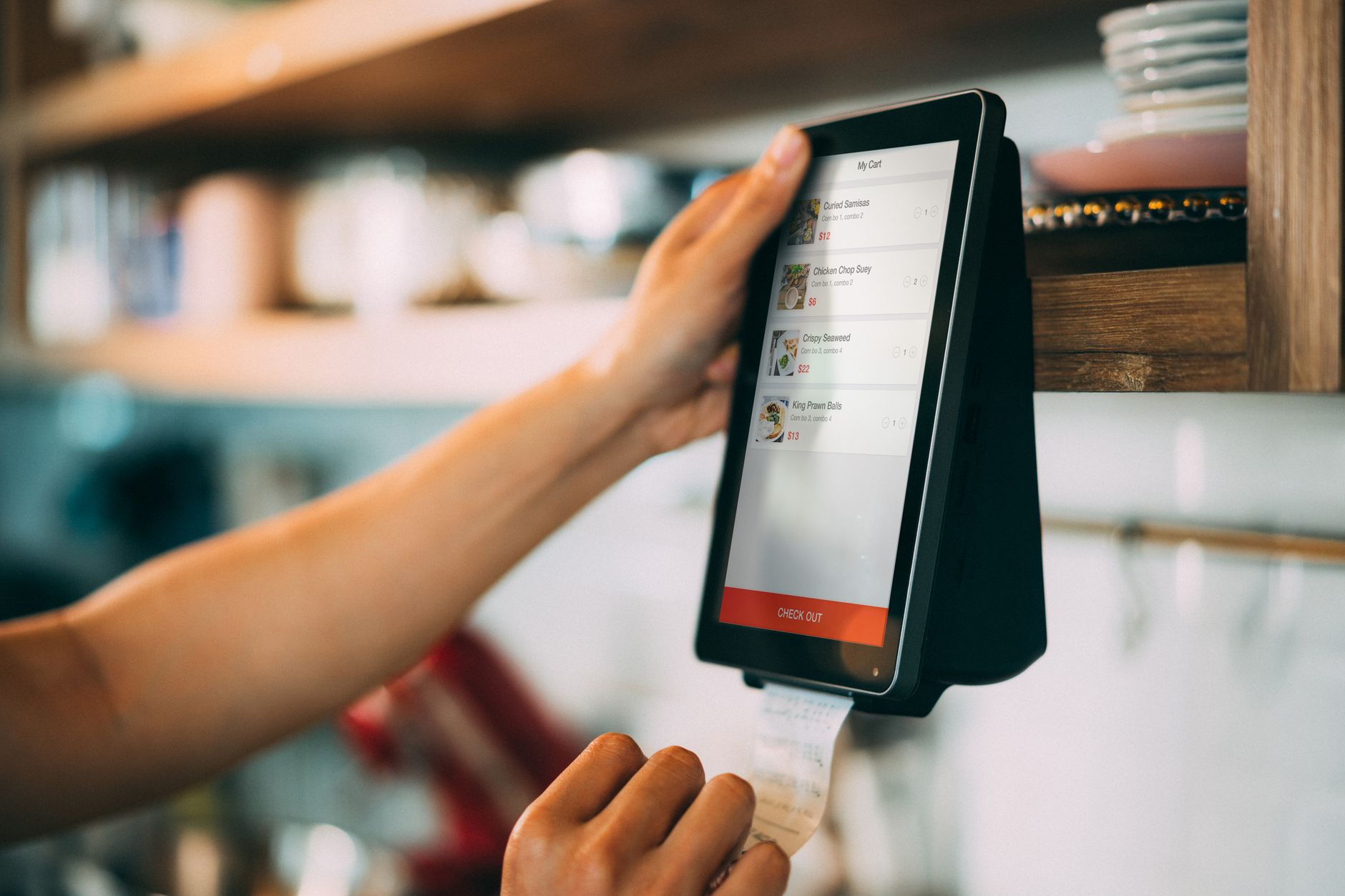 A hand uses a touchscreen digital payment system to process a receipt at a cafe.