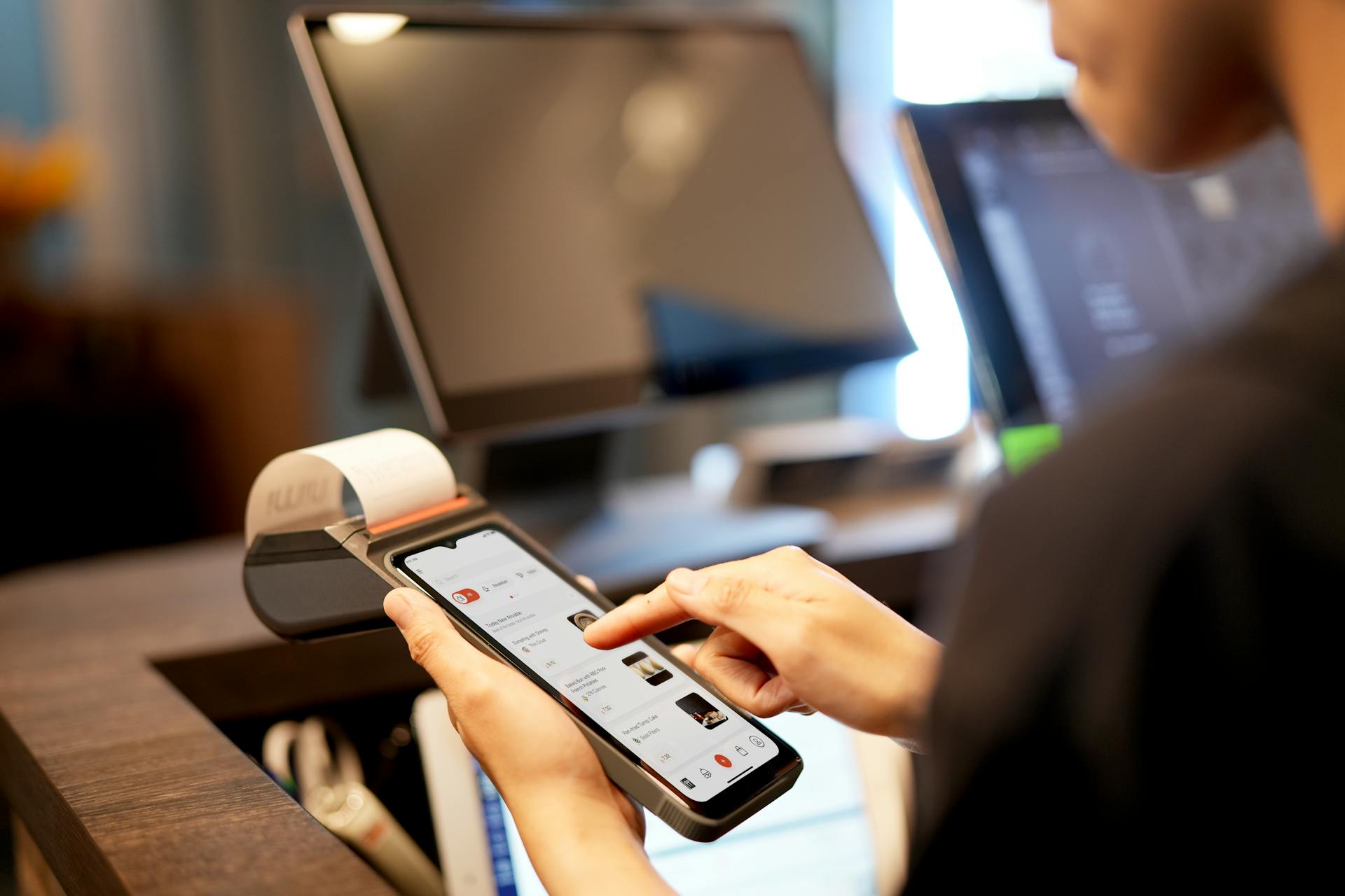 A person using a smartphone for payment at a modern POS terminal indoors.