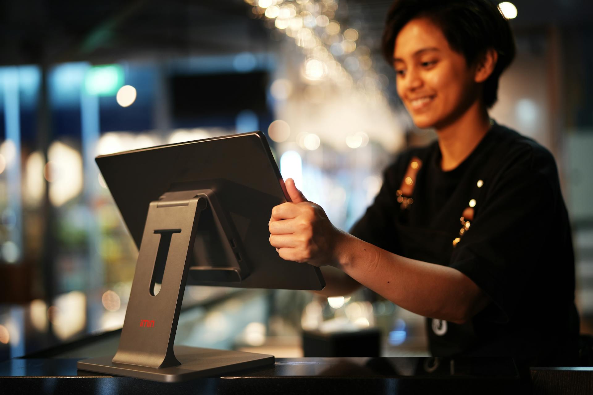 Smiling female cashier using a touchscreen in a modern restaurant setting.