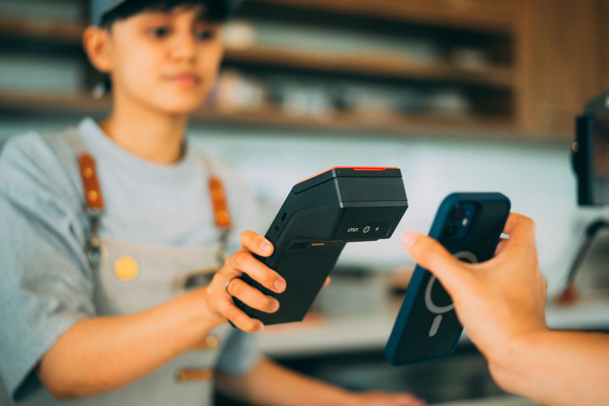 Vânzătoare cu terminal de plată portabil, în timp ce un client plătește cu telefonul