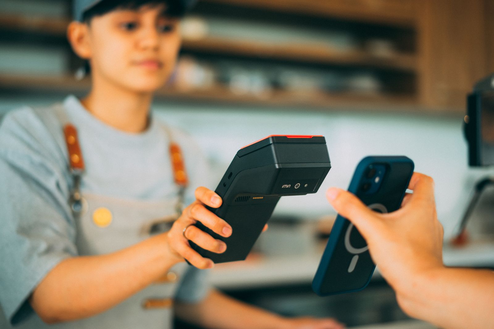 Shop worker holding a modern handheld card terminal toward a customer paying by phone