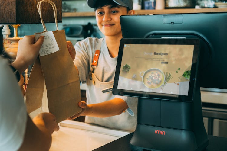 Smiling Employee Giving A Paper Bag With Receipt To A Customer